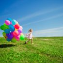 Little girl holding colorful balloons. Child playing on a green