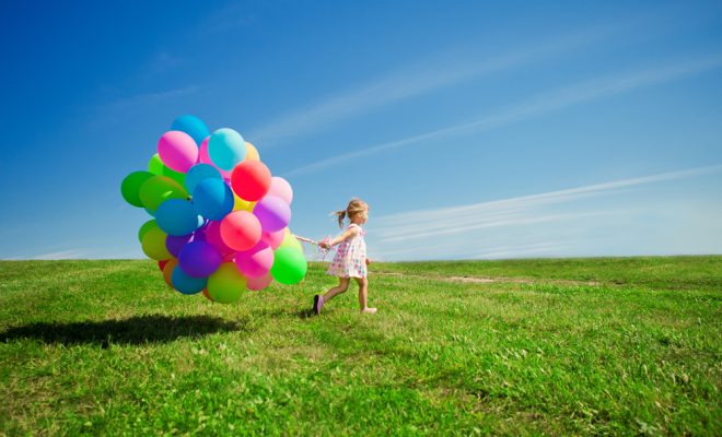 Little girl holding colorful balloons. Child playing on a green